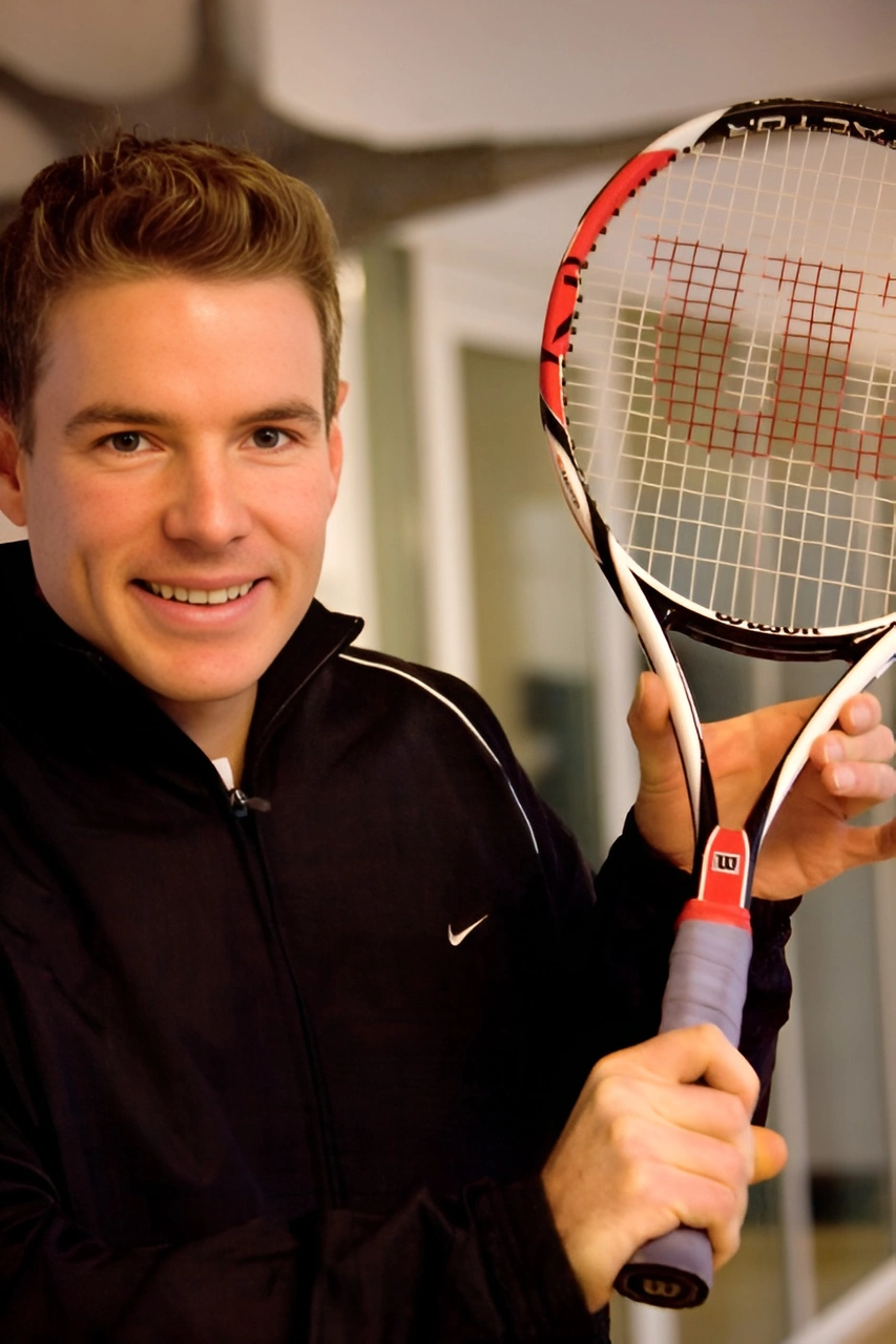 Christoph Kleinbeck smiling while holding a tennis racket representing Elite Coaching for high performance athletes.